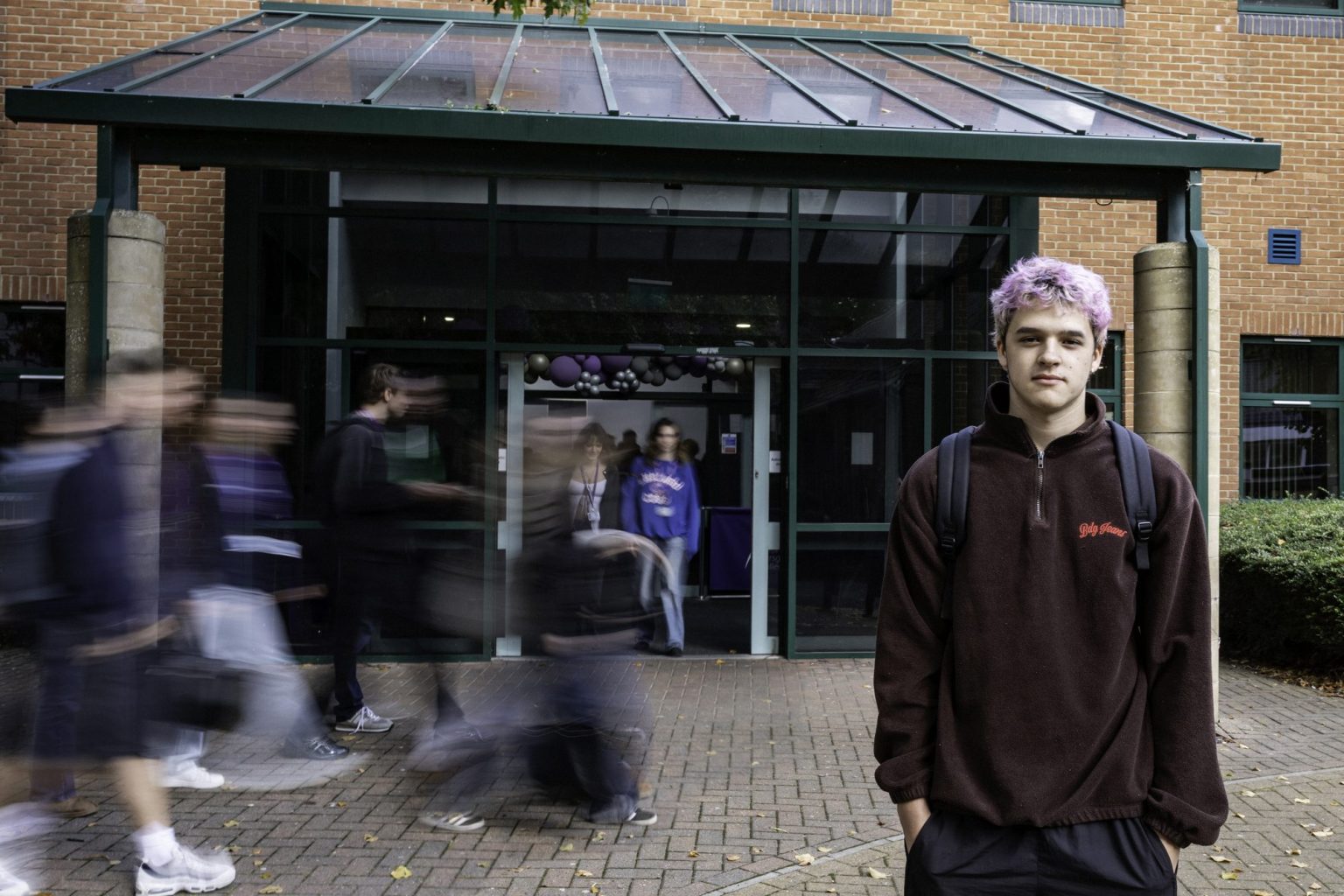 A student stands outside the college entrance at Prior Pursglove College while other students walk past