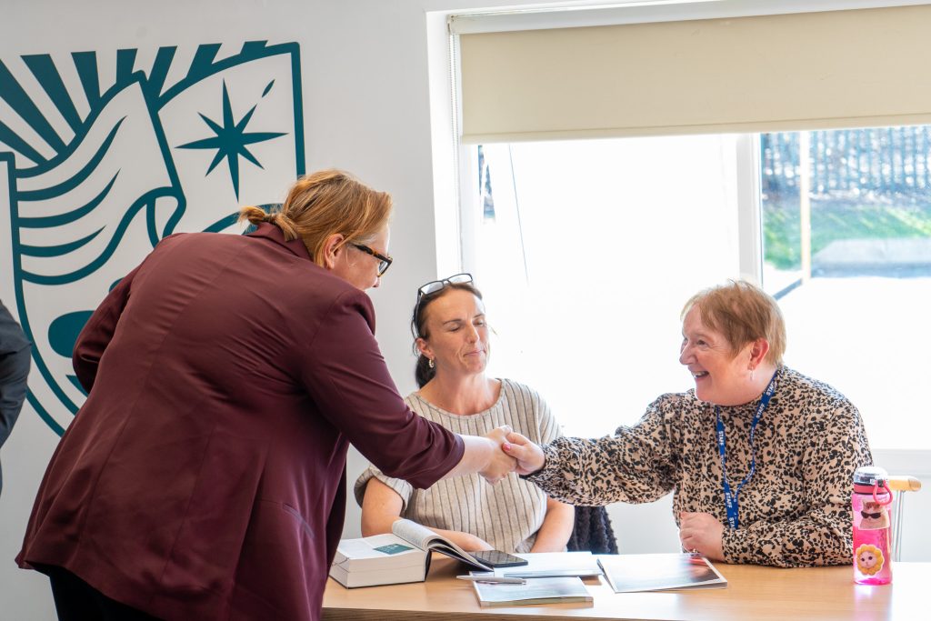 Anna Turley MP shakes hands with an adult learner at a classroom table at Whale Hill Primary School, with the Atomix logo mark on the wall behind