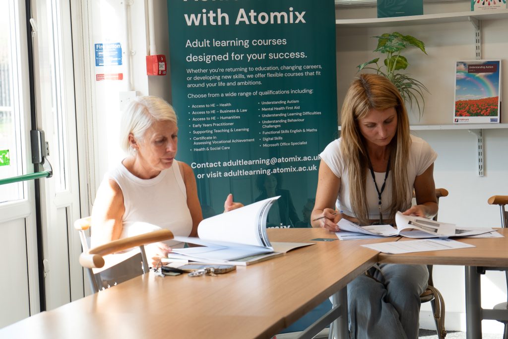 Two women look through course materials beside an Achieve with Atomix adult learning banner